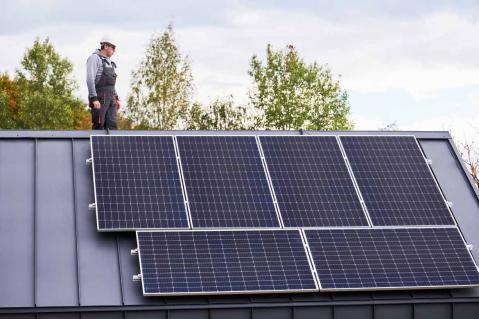 Techniker arbeitet an Photovoltaikanlage und steht auf Dach eines Hauses