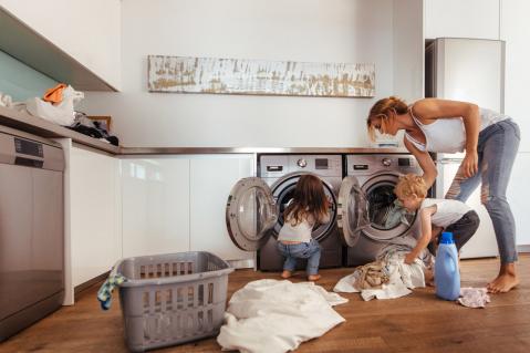 Frau füllt mit Kindern Wäsche in eine Waschmaschine