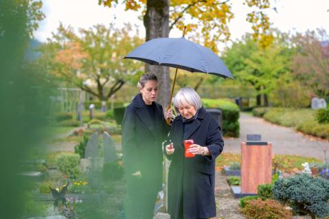 Zwei Frauen auf einem Friedhof mit einer Kerze in der Hand