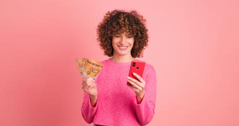 Frau vor rosa mit Geldscheinen und Handy in der Hand